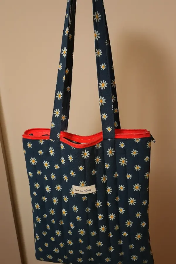 Bolsa tote de lona estampada con margaritas blancas sobre azul marino. Bolso de hombro grande y resistente con cremallera roja. Estilo casual y vintage.
