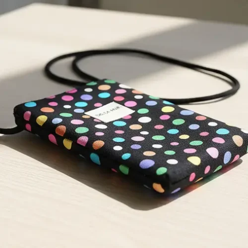 Bolso mini bandolera porta móvil con lunares de colores sobre fondo negro. Accesorio ligero y divertido para llevar el teléfono y tarjetas.